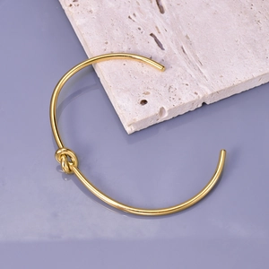 Elegant gold knot open bangle in minimalist stainless steel on a beige stone surface