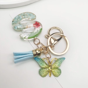 Detail view of resin letter S keychain with real dried flowers, blue tassel and butterfly