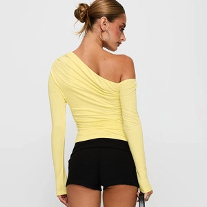 Détail du haut jaune pâle à une épaule et manches longues montrant la texture plissée