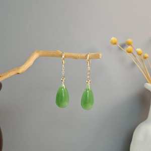 Close-up of green teardrop earrings hanging on natural wood with a minimalist background