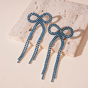 Détail de boucles d'oreilles nœud en strass bleu foncé avec pompons sur marbre