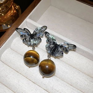 Detail view of butterfly studs with large tiger eye stone beads on a jewelry tray