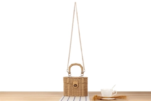 Detail of woven straw handbag featuring gold metal chain strap and turn-lock closure