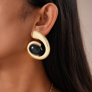 Close-up of golden wide spiral earrings with large black oval gemstone on model