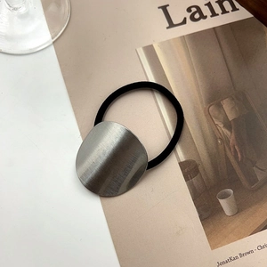 Minimalist elastic hair tie with a round brushed silver metal piece on a magazine background
