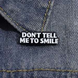Creative enamel pin with text Don't Tell Me To Smile on blue denim jacket