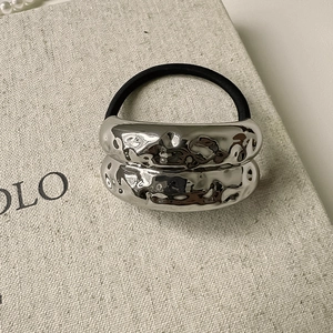 Detail of silver textured metal charm on elastic hair tie with mirror reflection