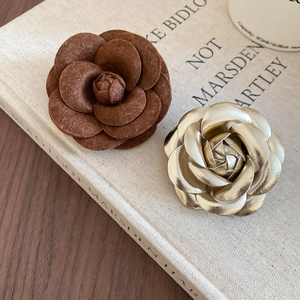 Detail of camellia brooches in brown felt and champagne gold on a minimalist background