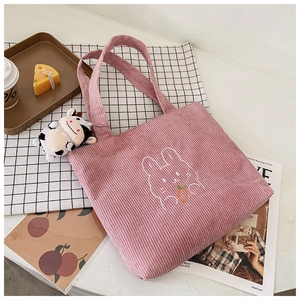 Detail of pink corduroy tote bag featuring rabbit embroidery and a plush cow pendant