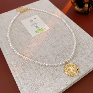 Détail du pendentif œil doré avec zircons colorés et collier de perles blanches