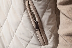 Close-up of diamond-quilted beige jacket showing metal zipper and fleece pocket lining