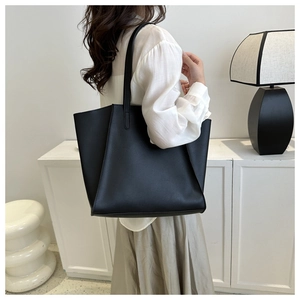 Detailed side view of a large black minimalist leather tote bag worn by a model