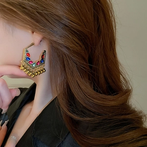 Detailed view of ethnic gold earrings with colorful stones and tassels on model