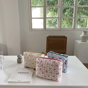 Close-up of three quilted makeup bags in floral and plaid patterns on a white table