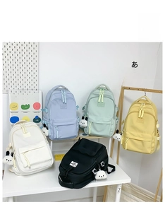 Five assorted colorful school backpacks with cute plush puppy charms in a lifestyle setting