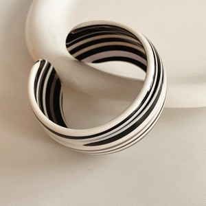 Detail view of a minimalist black and white striped acetate open cuff bracelet on a tray