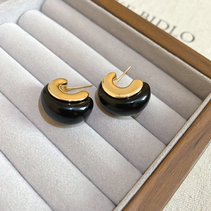 Detailed macro view of 18k gold plated C-shaped resin earrings in a grey jewelry box