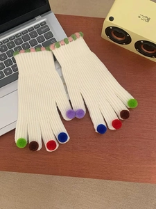 Dettaglio di guanti in maglia crema con piccoli pompon colorati su ogni dito