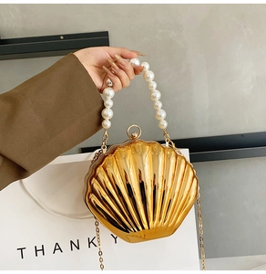 Detail of a golden shell-shaped clutch with a pearl handle and metallic chain strap