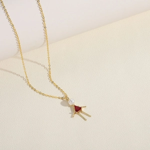 Detail of a gold necklace featuring a pearl and red triangular gem in a doll silhouette