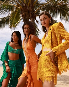 Tre modelle che indossano completi estivi in pizzo colorato su una spiaggia tropicale