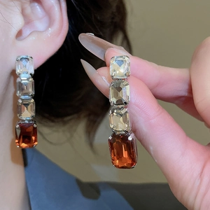 Model wearing square crystal drop earrings with clear gems and amber stone accents