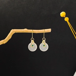 Detail of gold leaf earrings with white translucent ring and green gemstone accents