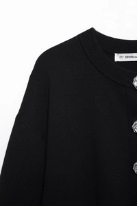 Detail of black knit cardigan showing silver buttons and crew neckline texture