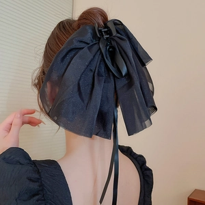 Détail d'une grande pince à cheveux avec nœud noir portée par une femme vue de l'arrière