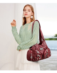 Detail view of burgundy faux leather handbag with multi-zipper and metallic ring decor