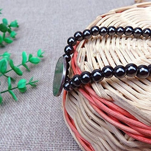 Pulsera elástica de hematita con colgante de jade verde sobre una cesta tejida