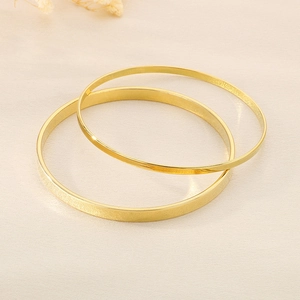 Close-up of dual gold titanium steel bangles with smooth finish on beige velvet background