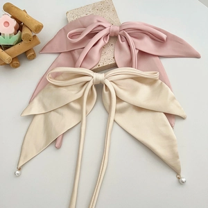 Close-up of pink and beige satin bow hair clips with long ribbons and pearl pendants