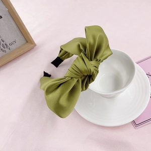 Close-up of a green satin knotted headband resting on a ceramic cup in a soft setting