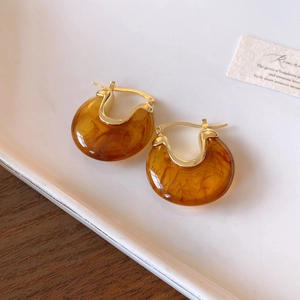 Close-up of amber resin C-shaped hoop earrings with gold metal posts on a ceramic tray
