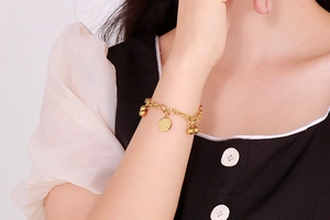 Dettaglio di bracciale dorato vintage con ciondolo a moneta e perline indossato al polso
