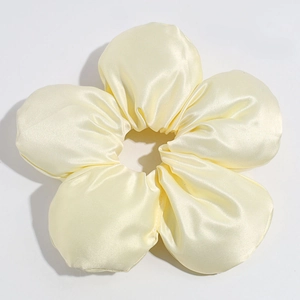 Detail view of a bright yellow satin flower scrunchie with smooth silk texture