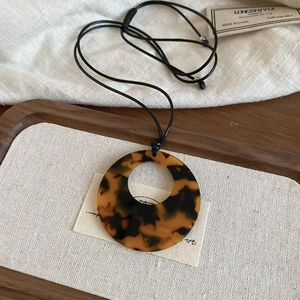 Close-up of a tortoiseshell resin round pendant necklace with a black cord on a wooden tray