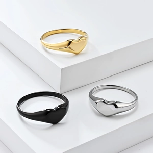 Minimalist heart-shaped rings in gold, black, and silver finishes on geometric stands