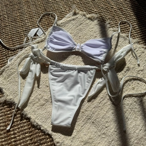 Detailed flat lay of white two-piece bikini with metallic buckle and bow tie side details
