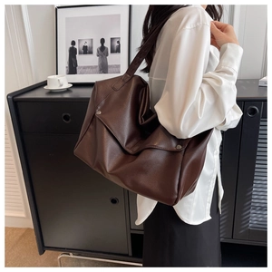 Detail of large brown tote bag showing premium litchi texture and side metal buckle design