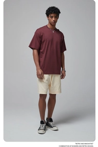 Male model wearing oversized maroon cotton T-shirt and beige drawstring shorts in studio