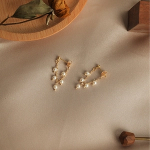 Elegant gold pearl earrings with wheat tassel chain design on silk background