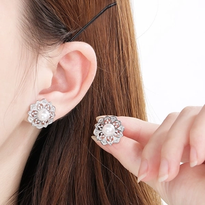 Detailed view of silver flower earrings with white pearls worn by a model in soft light