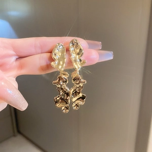 Detailed close-up of golden abstract fluid earrings with a high-gloss metallic finish