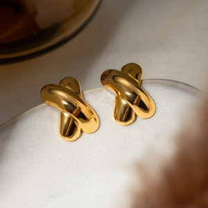 Macro detail of high-polish 18k gold X-shaped crisscross stud earrings on white ceramic