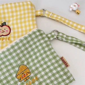 Detail of yellow apple and green cheese embroidery on checkered cotton zip pouches