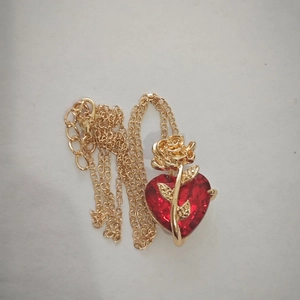 Close-up of red heart pendant with golden rose detail on a gold chain necklace