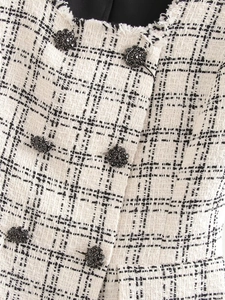 Close-up of black and white tweed fabric with fringe edges and flower-shaped buttons