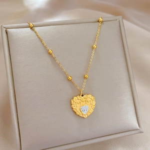 Detail view of a gold heart pendant with MM engraving and crystal on a beaded chain